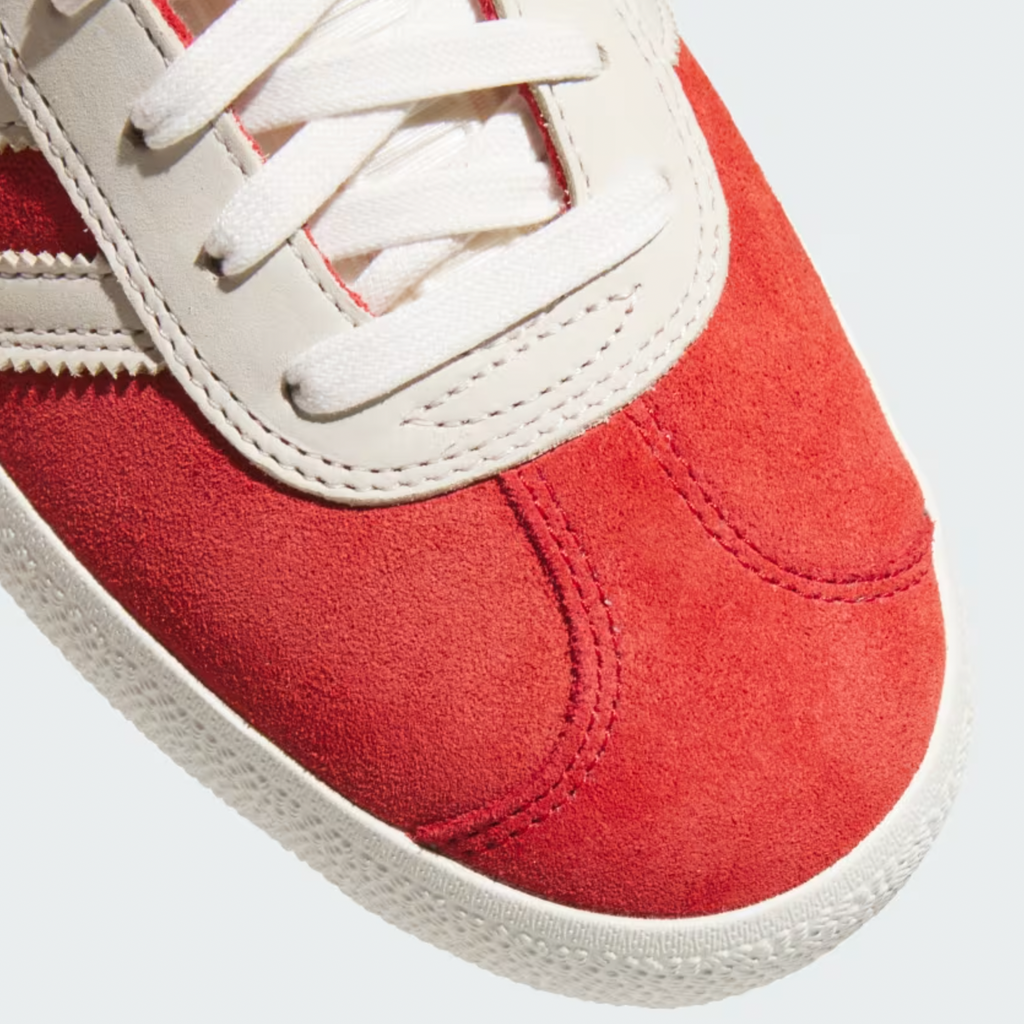 Close-up of an ADIDAS GAZELLE ADV in Better Scarlet and Chalk White, showcasing red suede with white leather accents and laces, set against a grey background.