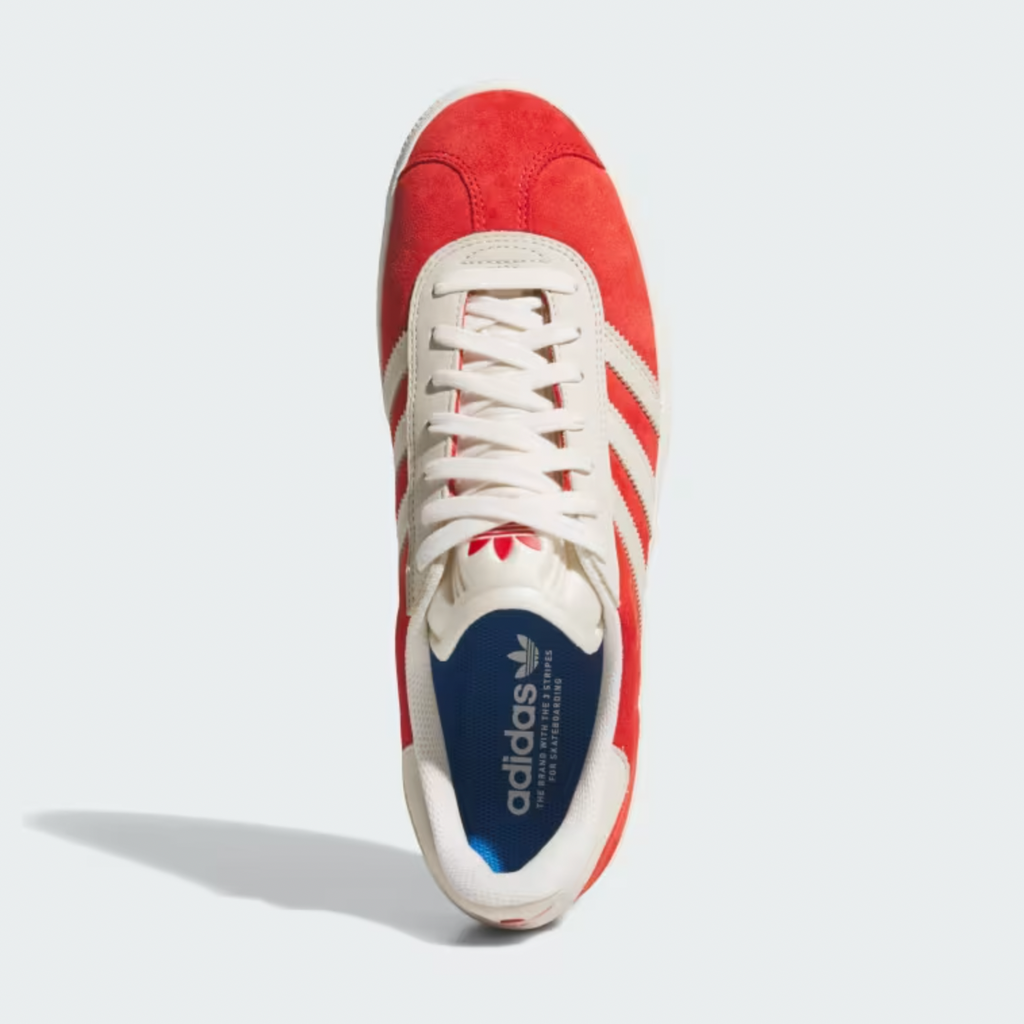 The ADIDAS GAZELLE ADV BETTER SCARLET / CHALK WHITE sneaker from Adidas, with its red and white design, mirrors the iconic Gazelle ADV style. It includes white laces and blue interior branding, offering a sporty look from above.