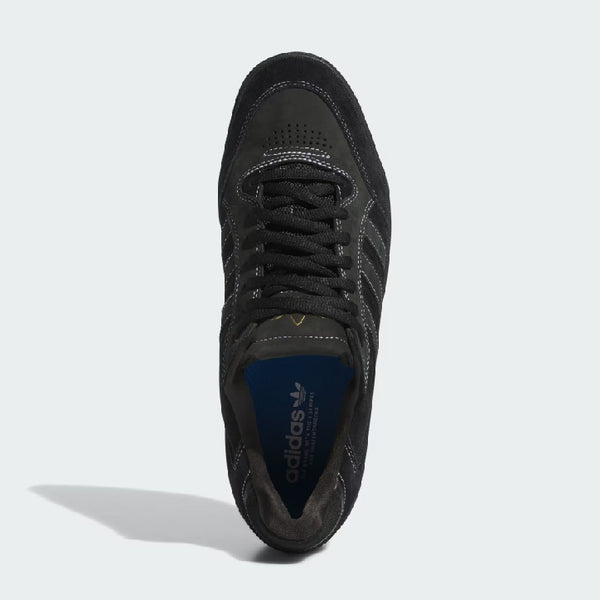 Top-down view of a single black ADIDAS Tyshawn Low Black / White / Gold Metallic skateboarding shoe with dark laces and a visible blue interior label.