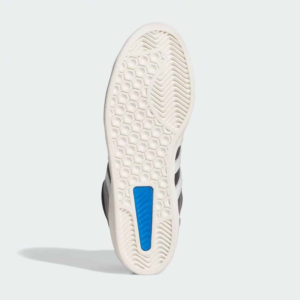 The image displays the sole of the ADIDAS SUPERSKATE ADV CORE BLACK / CRYSTAL WHITE / OFF WHITE, featuring a hexagonal tread pattern, blue rectangular insert, and curved grooves at the toe and heel.