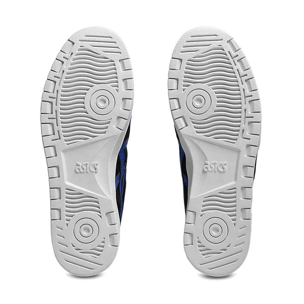 The image displays the soles of ASICS JAPAN PRO BLACK / BLUE skateboarding shoes, showcasing circular grip patterns with the ASICS logo embossed in the center, crafted from durable suede for enhanced resilience.