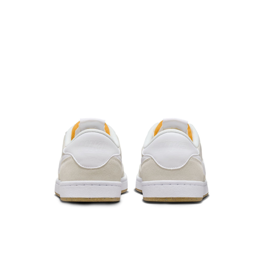 Rear view of the NIKE SB FC CLASSIC sneakers in summit white with tan soles, highlighted by orange accents around the heel, embodying the classic NIKE SB style.