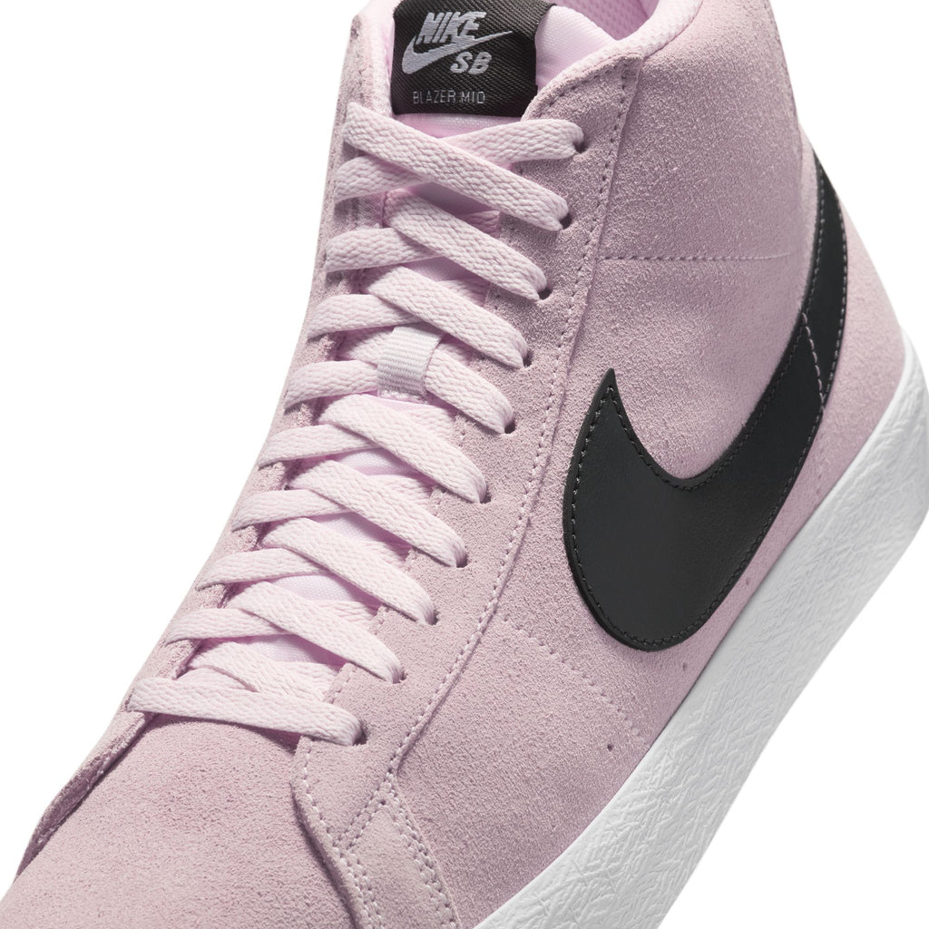 A close-up of the Nike SB Blazer Mid in Pink Foam/Anthracite-White-Gum Yellow, featuring a light pink suede upper, black Swoosh logo, and white sole.