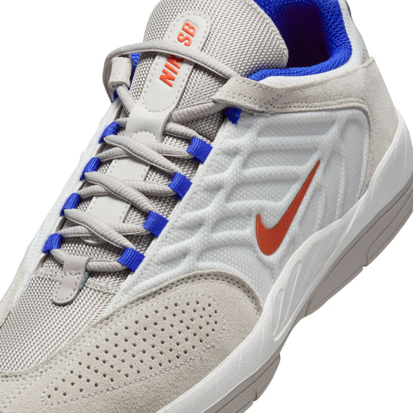 Close-up of a gray and white Nike SB Vertebrae Summit White/Cosmic Clay sneaker with orange logo, blue accents, and enhanced durability.