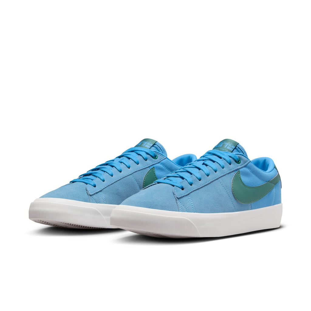 A pair of Nike SB Blazer Low Pro University Blue / Bicoastal skateboarder shoes with a blue upper, a white vulcanized construction sole, and green logo on a white background.