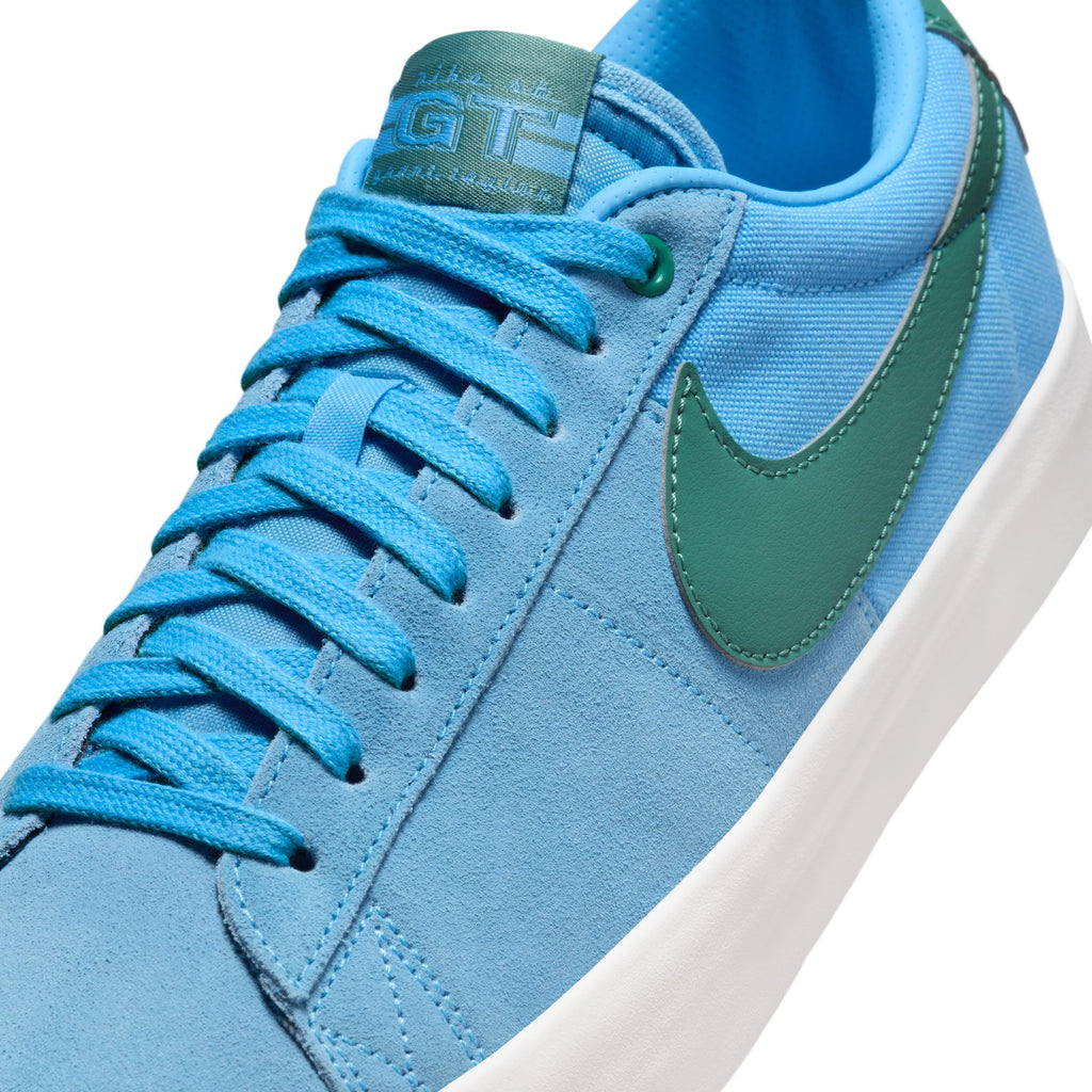 Close-up of a blue Nike SB Blazer Low Pro University Blue/Bicoastal sneaker with green Nike Swoosh and white vulcanized construction sole.