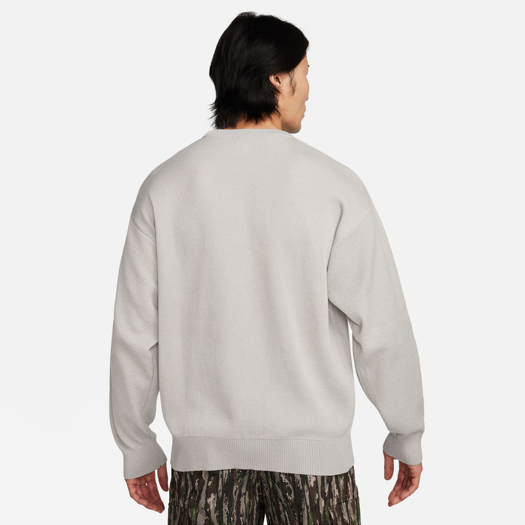 The back view of a man wearing a nike SB 'CITY OF LOVE' KNIT SWEATER GREY / LIGHT IRON.