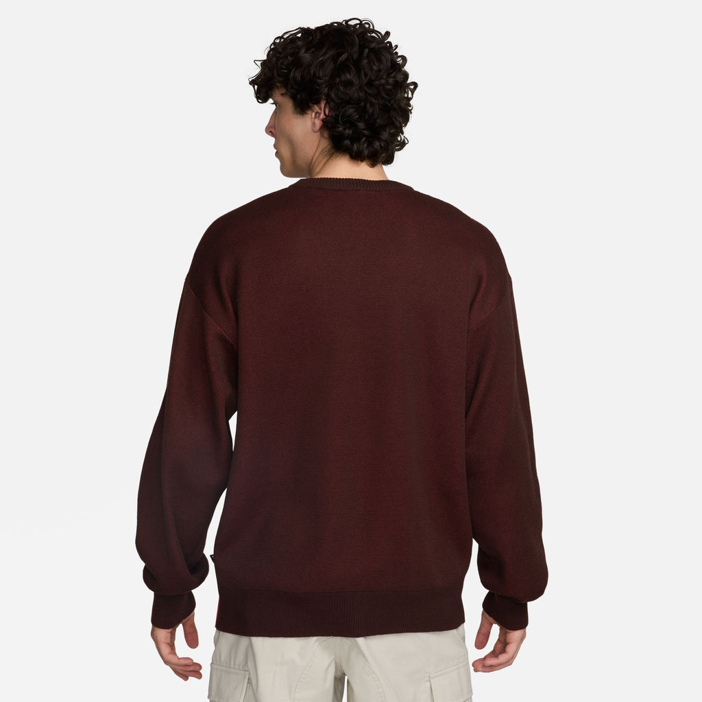 The back view of a man wearing a NIKE SB 'CITY OF LOVE' KNIT SWEATER BROWN / EARTH with the phrase 'CITY OF LOVE' printed on it.