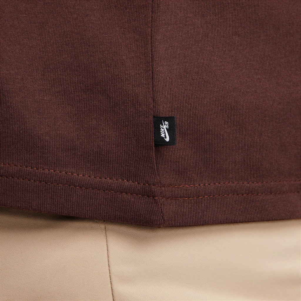 Close-up of a brown nike 'CITY OF LOVE' LS skate tee with a logo tag on the hem.
