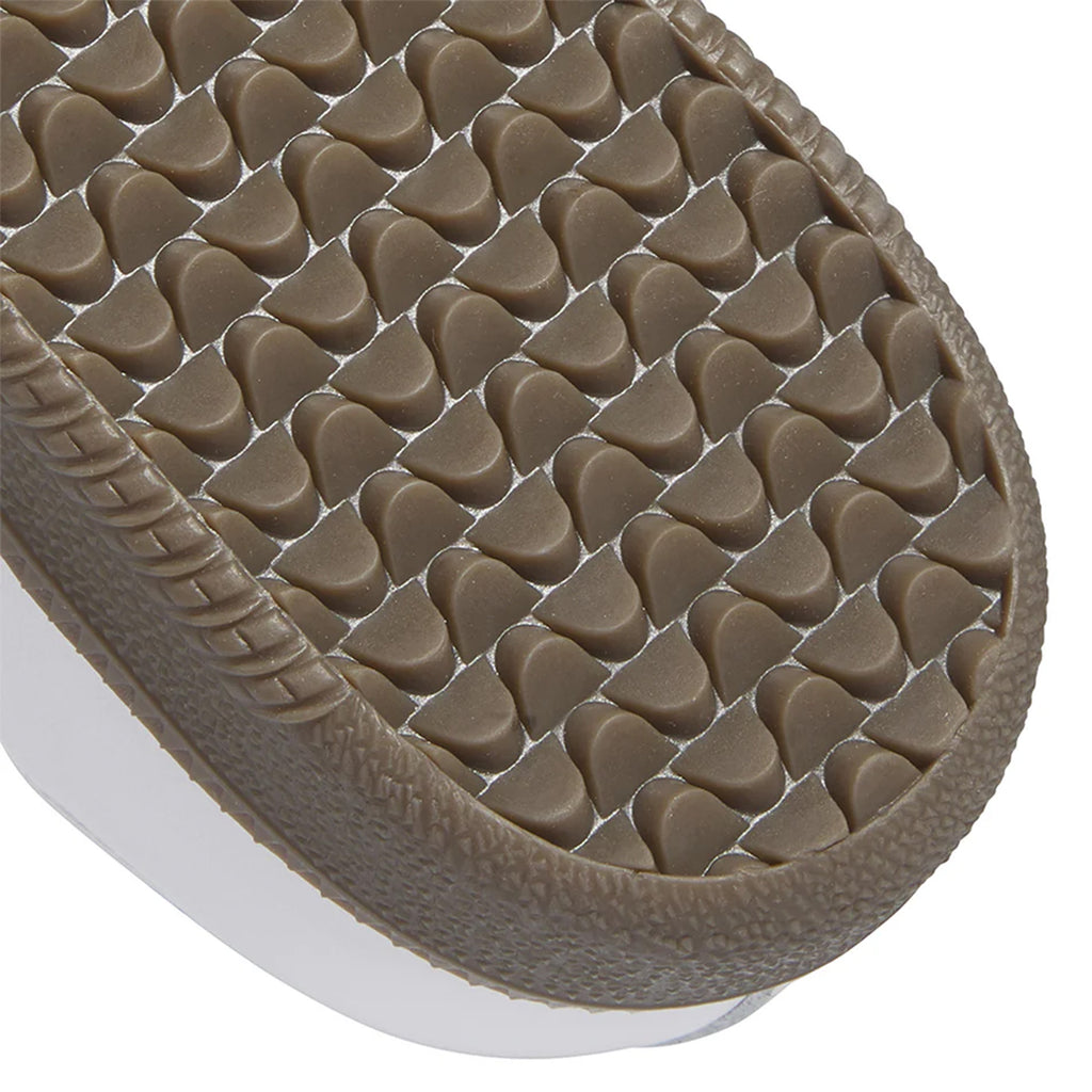 Close-up of a brown rubber sole with a textured, triangular pattern on the bottom edge of an adidas Samba ADV skateboarding shoe in Cloud White and Collegiate Purple, featuring Adituff toe reinforcement.