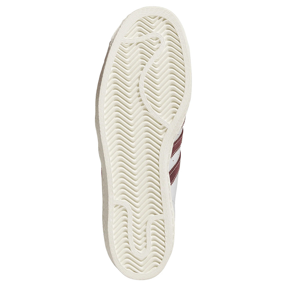 Bottom view of the ADIDAS SUPERSTAR 80 ADV in Crystal White/Shadow Red, showing a herringbone tread pattern and visible red stripes on the side.