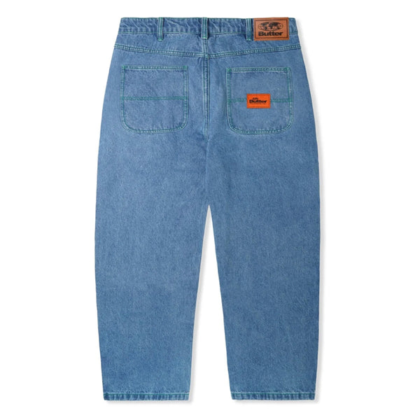A pair of BUTTER GOODS SANTOSUOSSO DENIM PANT WASHED INDIGO jeans with an orange patch on the back featuring contrast green stitching and washed indigo denim.