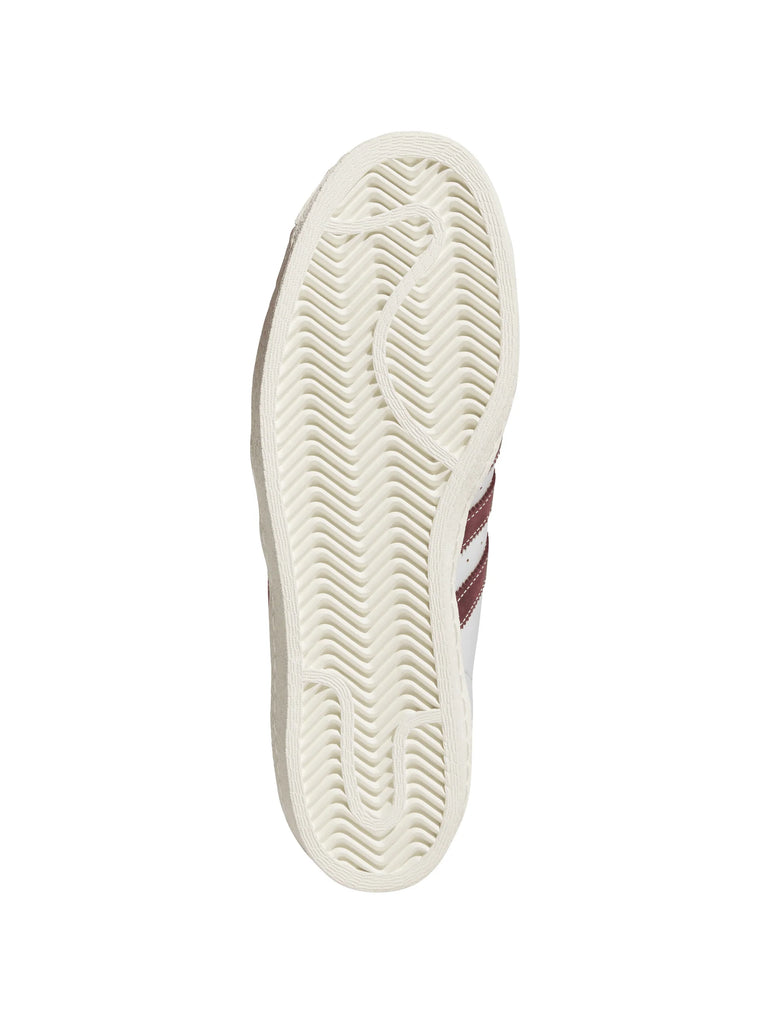 The image shows the sole of the ADIDAS SUPERSTAR 80 ADV CRYSTAL WHITE / SHADOW RED with a textured, wavy tread pattern and a shadow red stripe on the side.