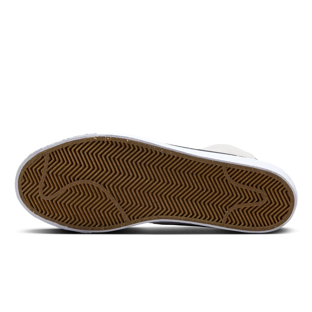 The image shows the sole of a NIKE SB BLAZER MID WOLF GREY / MIDNIGHT NAVY with a zigzag tread pattern on a brown rubber surface, featuring Zoom Air cushioning for added comfort.