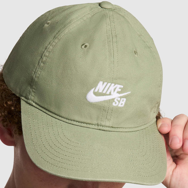 Close-up of a person holding a green Nike SB Club Hat Oil Green, focusing on the embroidered white logo on the front.
