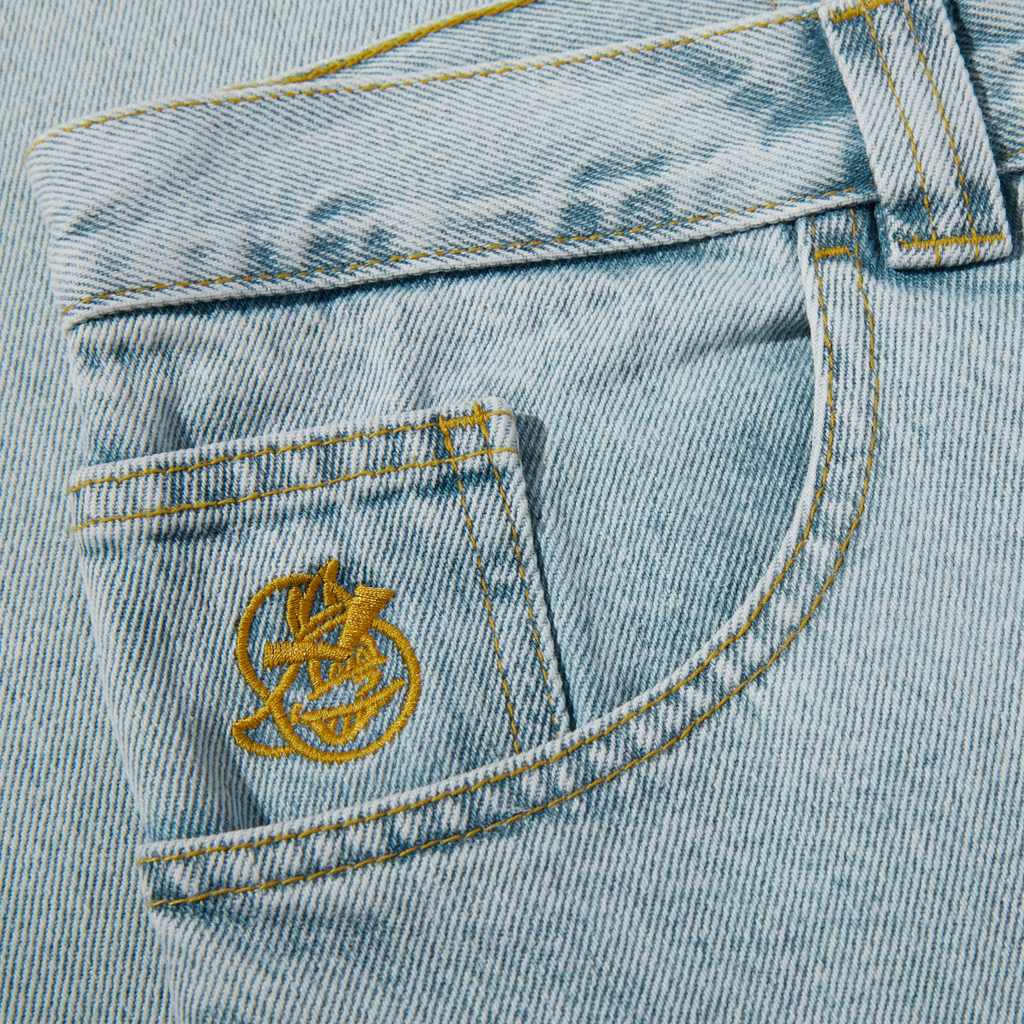 A close up of a POLAR '93! DENIM LIGHT BLUE pocket with a gold emblem on it, made from denim fabric.