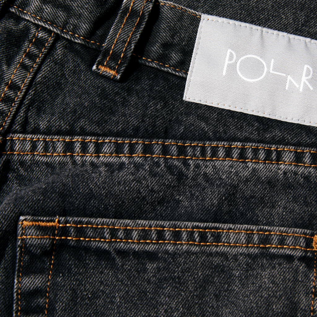 Close-up of a POLAR '89 denim washed black fabric with orange stitching and a white label displaying the brand "POLAR '89.