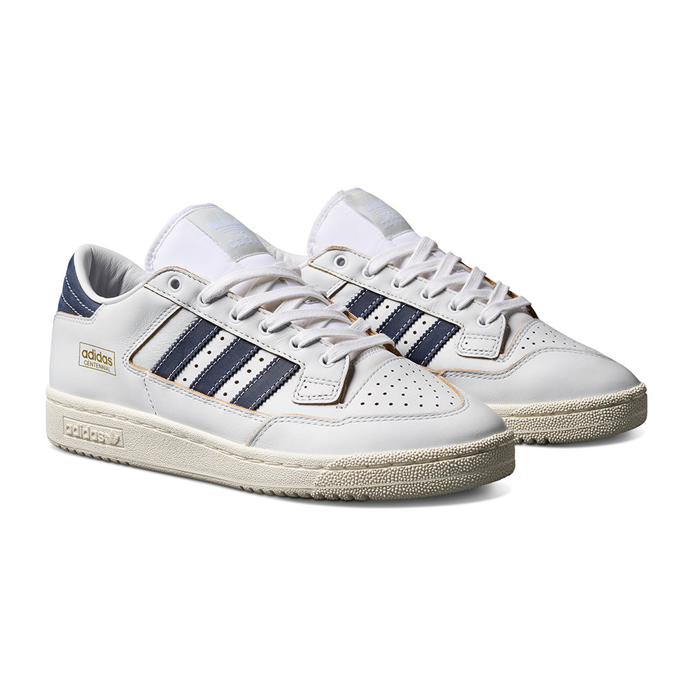 A pair of ADIDAS CENTENNIAL 85 LOW ADV in crystal white with shadow navy stripes, gold branding, off-white soles, and split suede accents is displayed side by side on a white background.