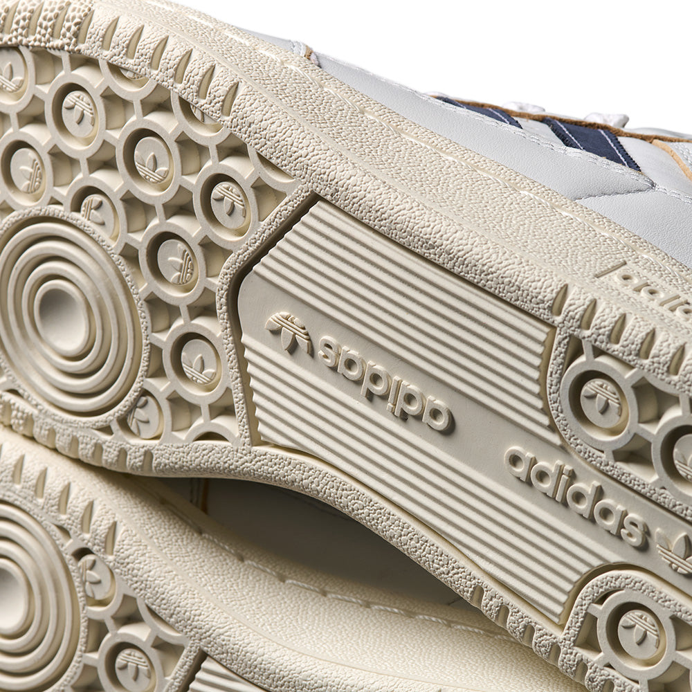 Close-up of the textured beige sole on the ADIDAS CENTENNIAL 85 LOW ADV CRYSTAL WHITE / SHADOW NAVY, featuring brand logo and circular tread for skateboarding, crafted in durable split suede.