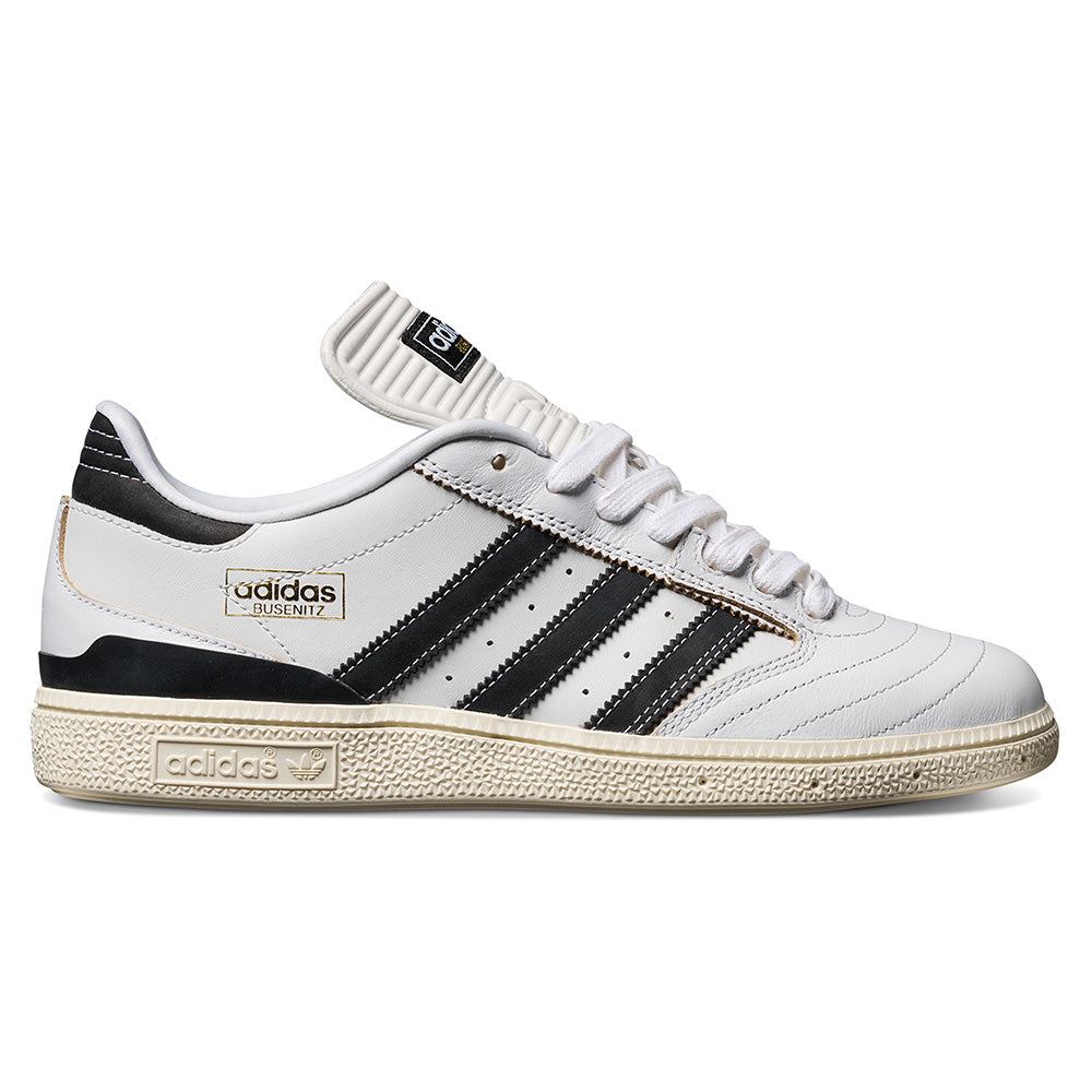 The ADIDAS BUSENITZ in Crystal White/Black/Off White, featuring black stripes, gold logo details, premium suede accents, and a textured beige sole, is shown in a side profile on a plain background.