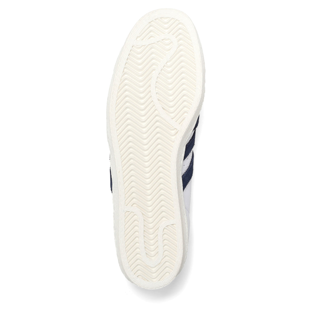 A white and navy ADIDAS X POP TRADING CO. SUPERSTAR ADV sneaker on a white background by Adidas.