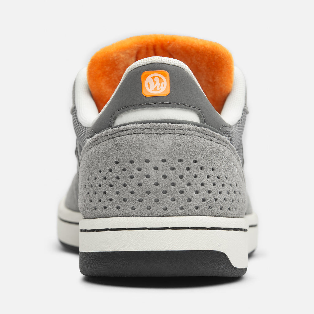 Rear view of a gray skate shoe with an orange inner lining and a distinctive circular logo on the pull tab, part of the NB NUMERIC x VU 440 V2 GREY / ORANGE collection.