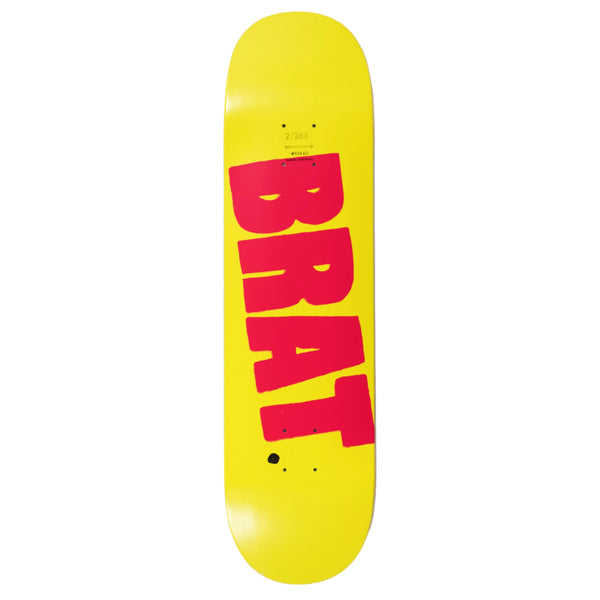A yellow skateboard deck with the Carpet Co. Brat Logo in large red letters screened printed vertically on the surface.