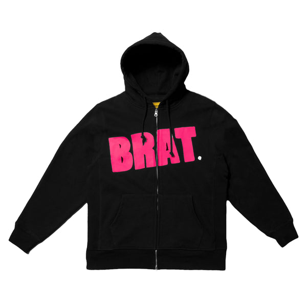A Carpet Co. black zip-up hoodie with the word "brat." in pink block letters across the chest, displayed on a mustard background.