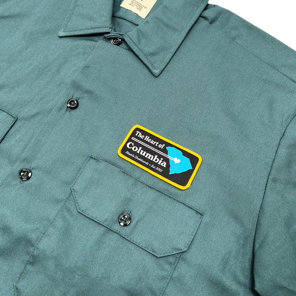 A Bluetile Skateboards "HEART OF COLUMBIA" work shirt in Lincoln Green with a yellow PATCH on it.