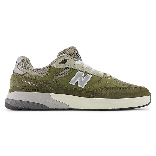 The NB NUMERIC REYNOLDS 933 GREEN by NB NUMERIC features an olive green and gray suede/mesh upper, white "N" logo, ABZORB midsole for comfort, and a white/gray rubber sole, shown in side profile.