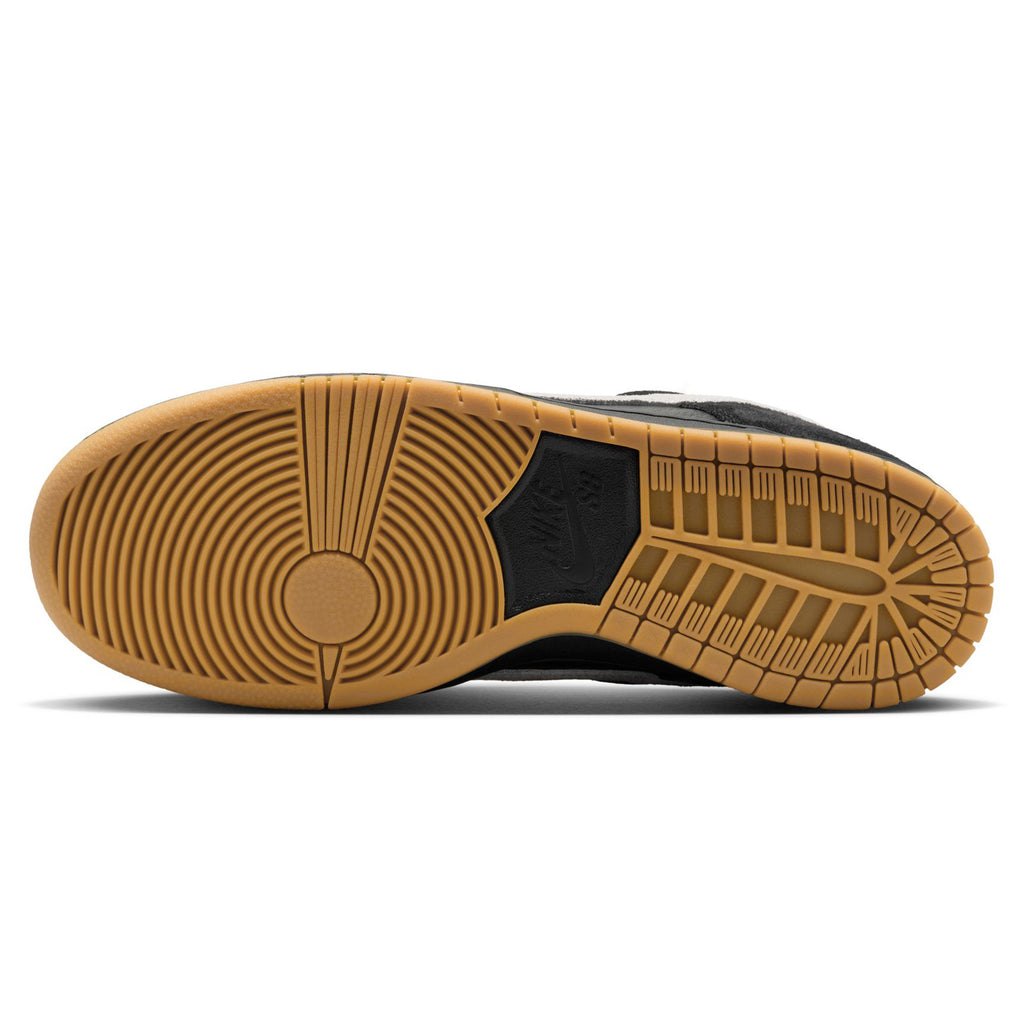 Sole view of a NIKE SB DUNK LOW PRO BLACK / WHITE-BLACK-GUM LIGHT BROWN shoe, showcasing a black and tan tread with geometric designs and textures, paired with a foam midsole for enhanced comfort.