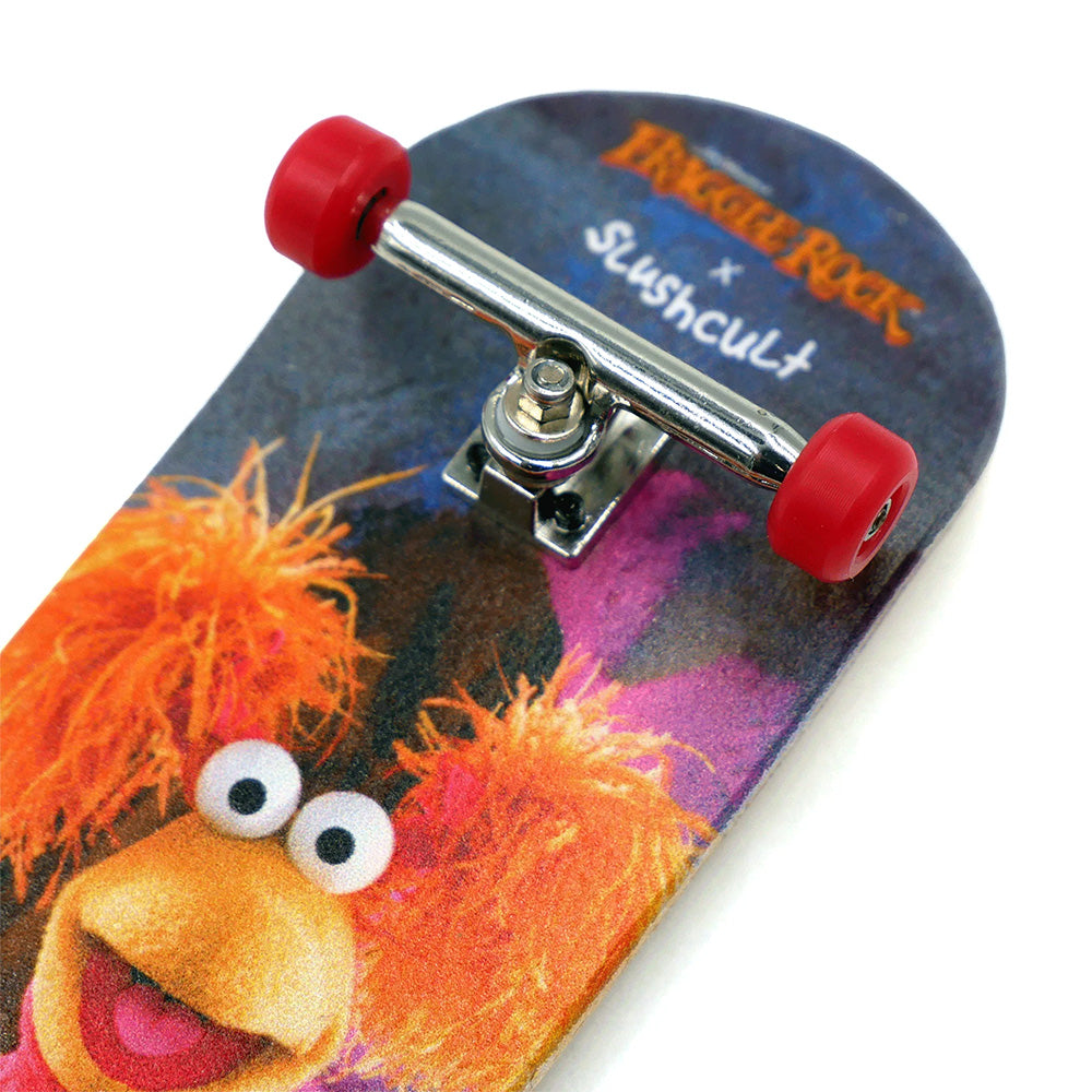 A close-up of the SLUSHCULT X FRAGGLE FINGERBOARD RED showcases a Fraggle Rock character, red wheels, and "SLUSHCULT X FRAGGLE" on the deck—perfect for fans and collectors.