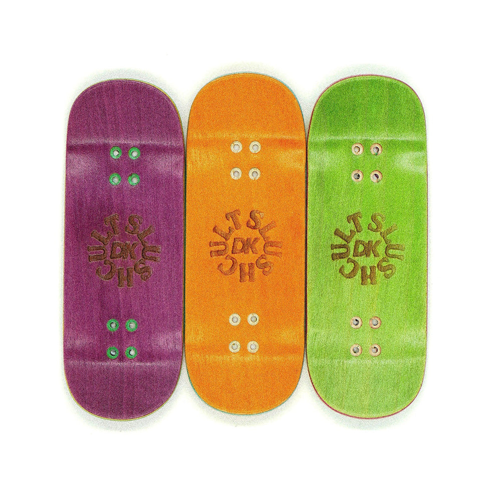 Three SLUSHCULT "MID EVIL" FINGERBOARD DECK 34MM in purple, orange, and green are displayed side by side, each with a central sun-shaped logo—a DK Fingerboards collab featuring a medium concave design.