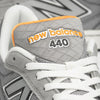 Close-up view of a gray NB NUMERIC x VU 440 V2 GREY / ORANGE skate shoe showing details of the logo, laces, and textured fabric.