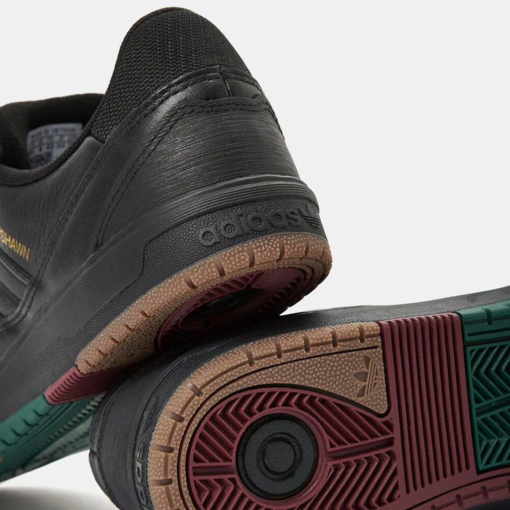 Close-up of two black ADIDAS TYSHAWN 2 BLACK / BLACK / GUM skateboarding shoes featuring multi-colored soles, highlighting the intricate tread patterns in red, green, and beige.