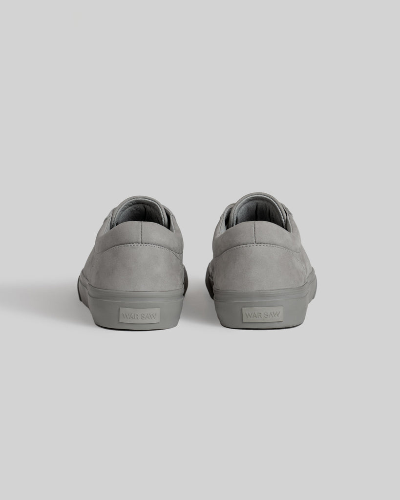 A pair of CHAPTER | STONE FG NUBUCK gray sneakers by WARSAW LTD, crafted in suede, are shown from the back on a light gray background with "WARSAW" displayed on the heels, exemplifying minimalistic design.