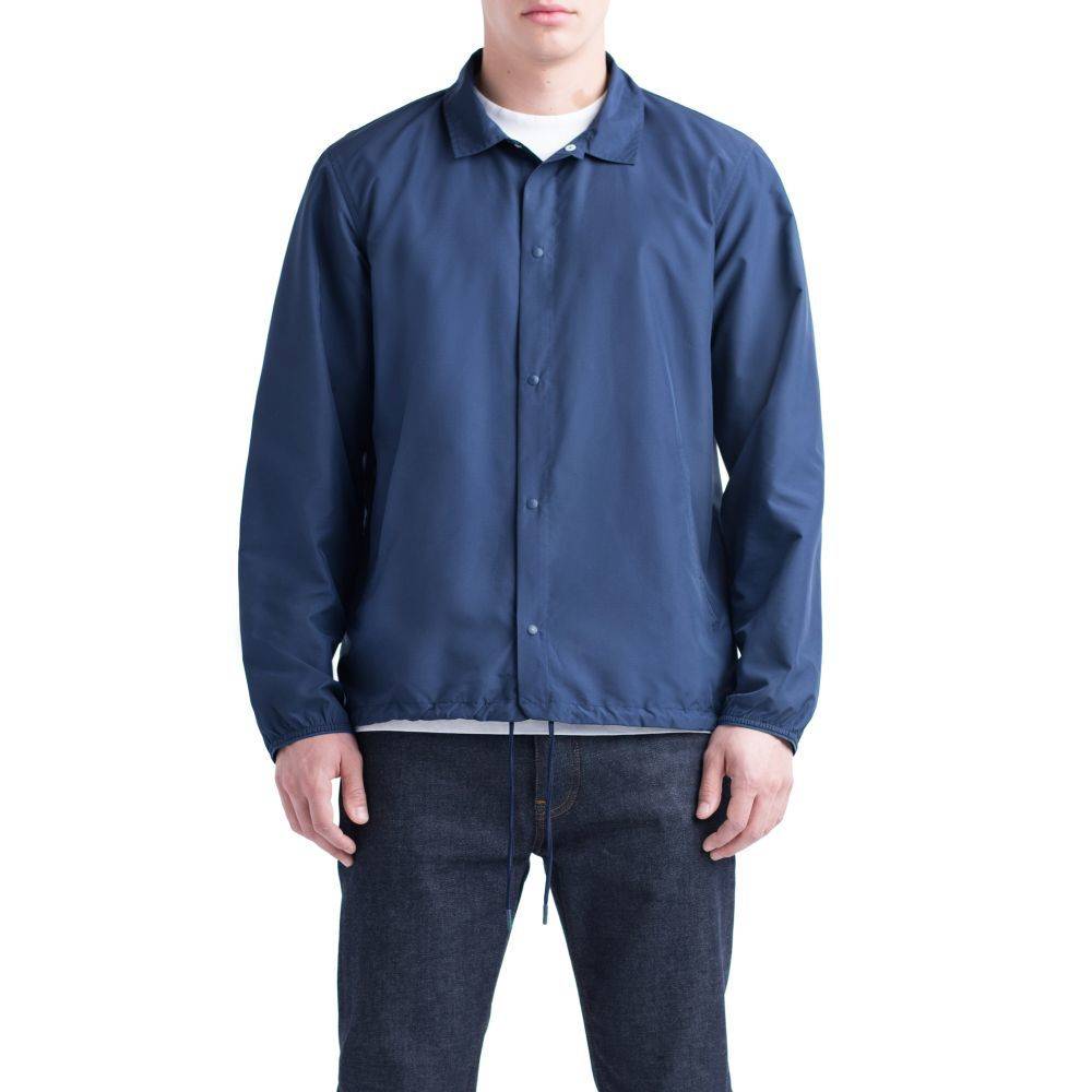 A person wearing a navy HERSCHEL SUPPLY CO VOYAGE COACH PEACOAT by HERSCHEL, made from water-resistant ripstop fabric, paired with dark jeans, stands against a plain white background.