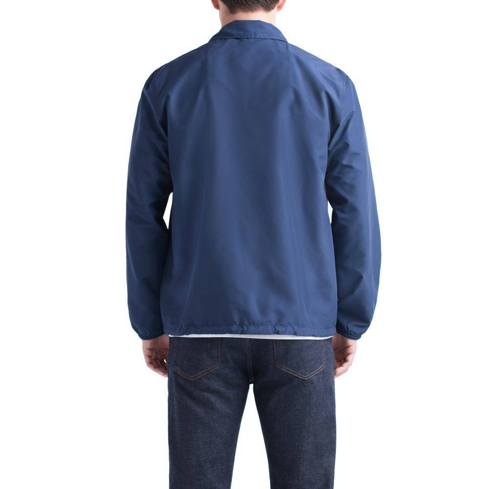 A person in a HERSCHEL SUPPLY CO VOYAGE COACH PEACOAT by HERSCHEL, made of water-resistant ripstop fabric, and dark jeans stands facing away from the camera against a plain white background.