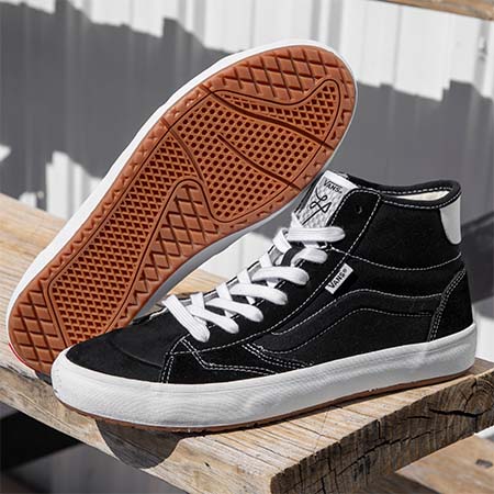 A pair of VANS THE LIZZIE BLACK / WHITE shoes sitting on top of a wooden bench.
