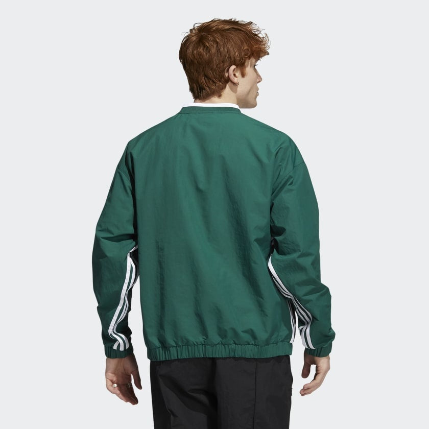 A person with short, curly hair is seen from behind wearing the ADIDAS WIND PULLOVER COLLEGIATE GREEN / WHITE and black pants, set against a plain background.