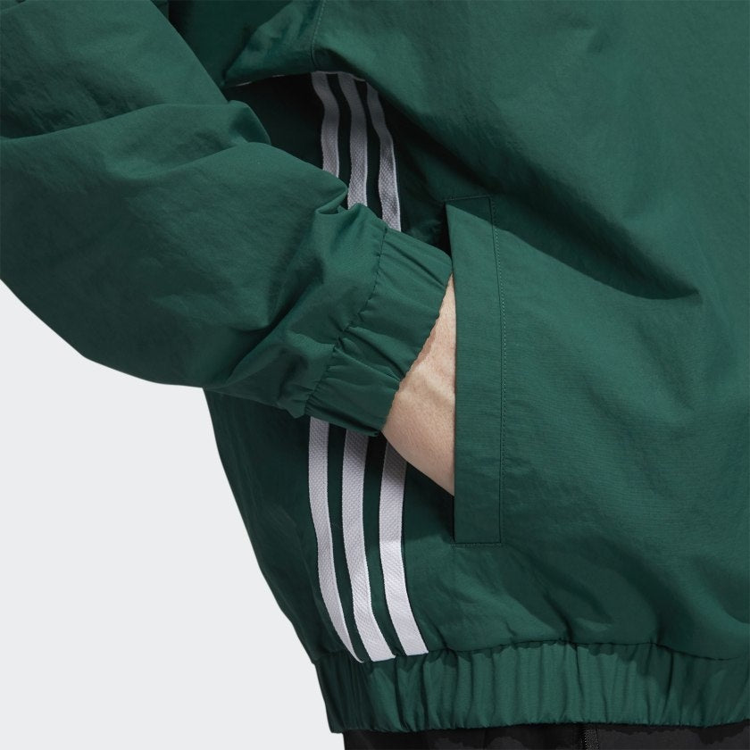 Close-up of a person wearing the ADIDAS WIND PULLOVER in Collegiate Green/White, with signature white stripes and one hand in the pocket.