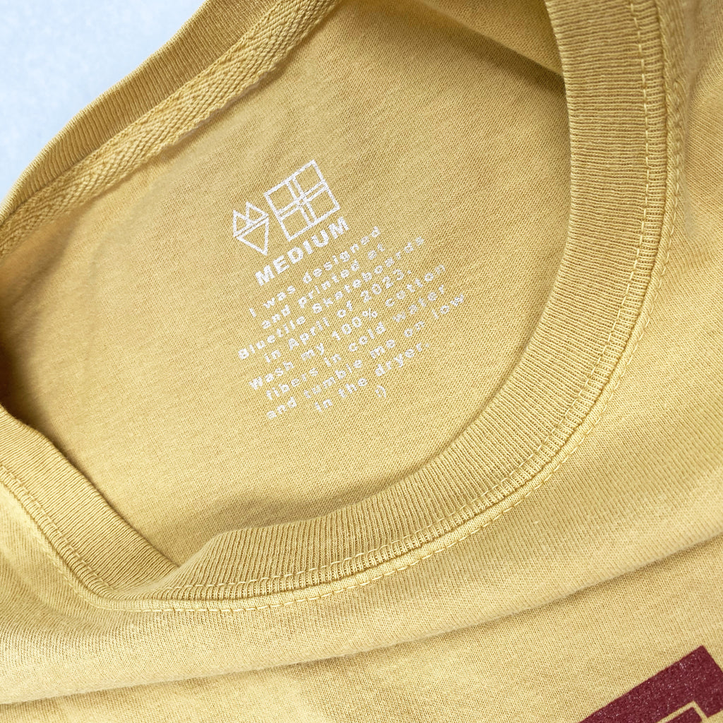 A close up of white tag print on the inside of the gold shirt
