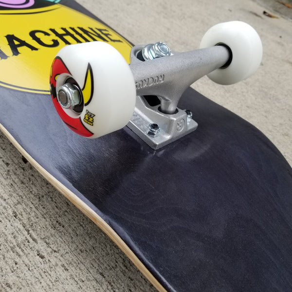 Close-up of a TOY MACHINE VENNDIAGRAM COMPLETE skateboard with red bearings, white wheels, and silver trucks on a concrete surface.