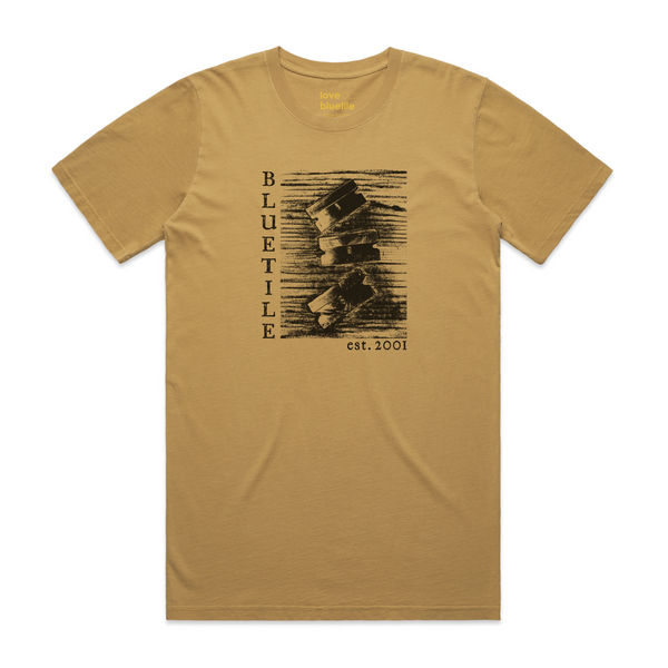 A Bluetile Skateboards BLUETILE "RAZORS" TEE FADED MUSTARD with an image of a man riding a bike.