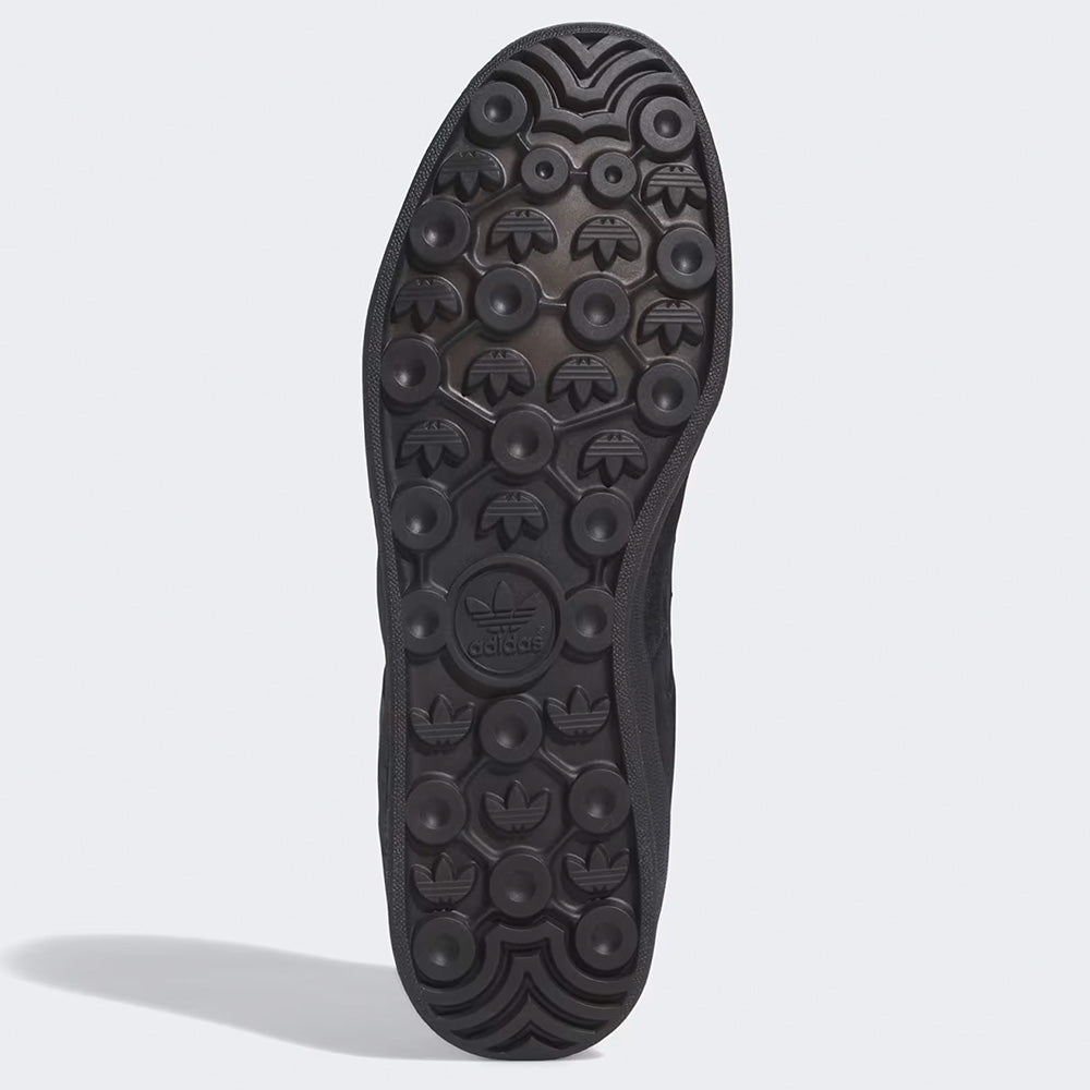 The image shows the black rubber sole of the ADIDAS GONZ ALOHA SUPER CORE BLACK / PRELOVED TEAL, featuring circular treads, multiple embossed Trefoil logos, and Adiprene cushioning for comfort.