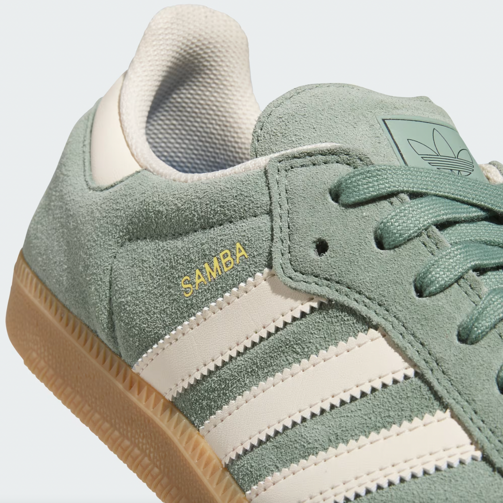 Close-up of an Adidas Samba ADV shoe in Silver Green, featuring Wonder White stripes, Adituff toe reinforcement for durability, a gum sole, and "SAMBA" lettering in gold—ideal for skateboarding enthusiasts.