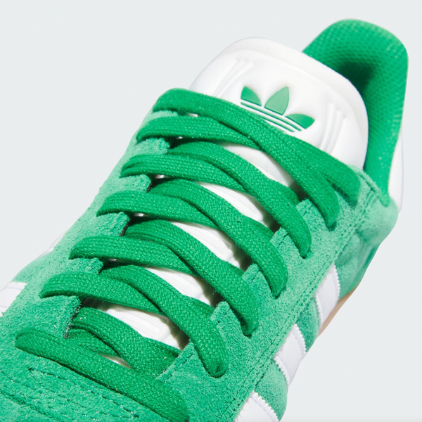 Close-up of an ADIDAS GAZELLE ADV in green, featuring matching laces, cloud white stripes, a logo on the white tongue, and a durable vulcanized rubber outsole for enhanced grip.