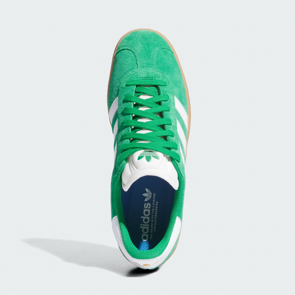 A green Adidas Gazelle ADV sneaker with water-repellent suede and cloud white stripes, viewed from above, features the brand's logo on the insole.