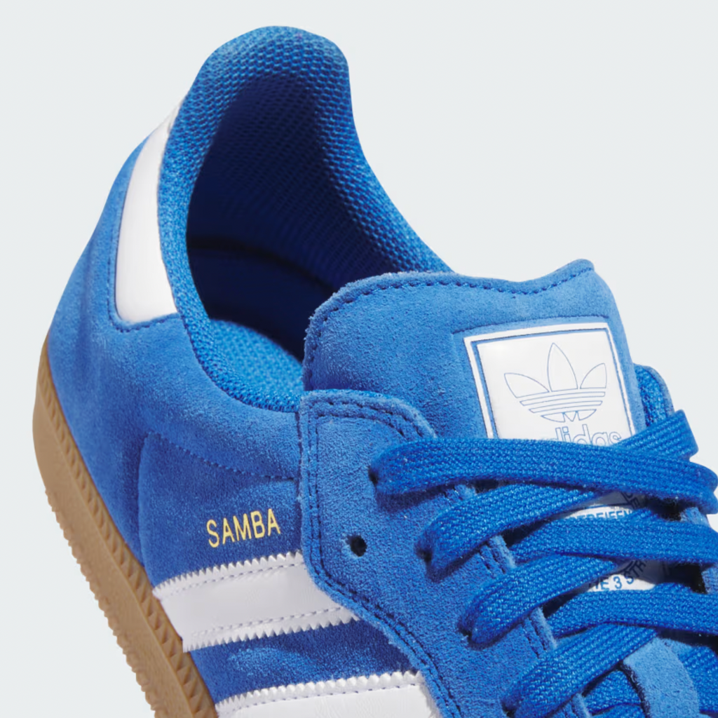 Close-up of an Adidas Samba ADV in Blue Bird/Cloud White, featuring "Samba" in gold metallic, Adituff toe reinforcement, and resting on a durable white gum sole.