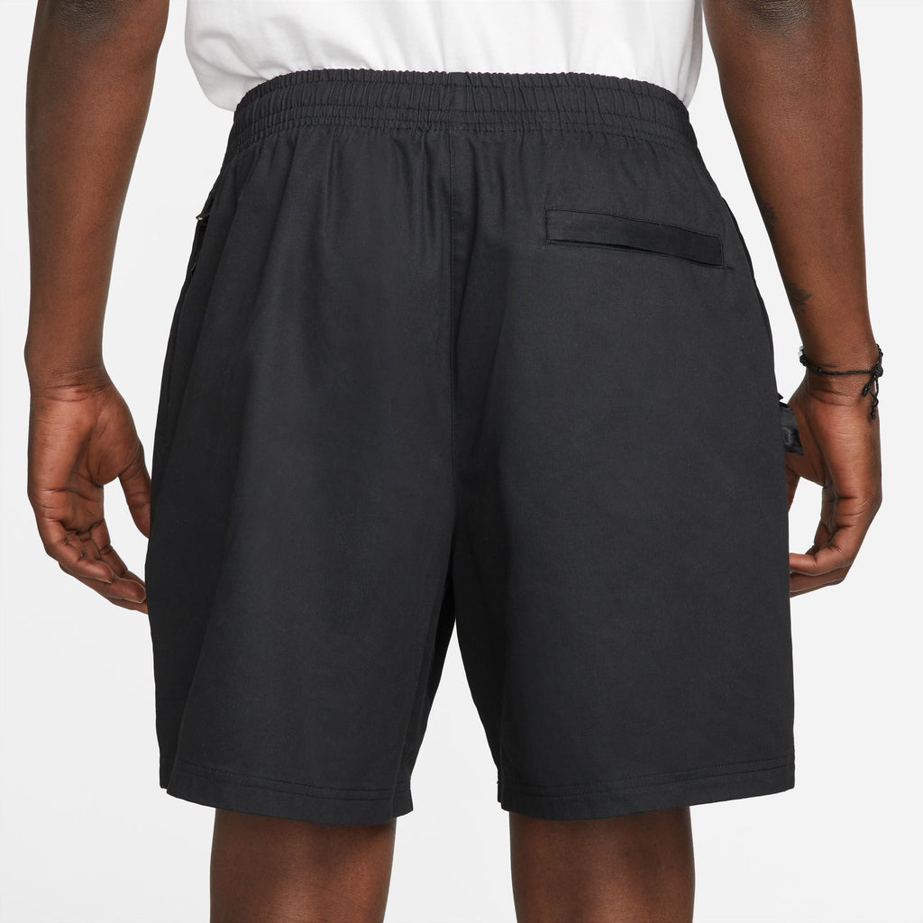 A man wearing a white shirt and black Nike SB Skyring skate shorts with a loose fit.